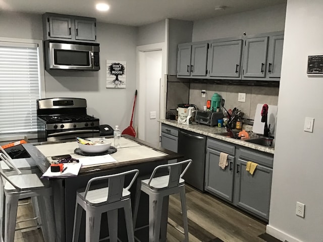 kitchen featuring a breakfast bar area, gray cabinetry, stainless steel appliances, dark wood-style flooring, and backsplash