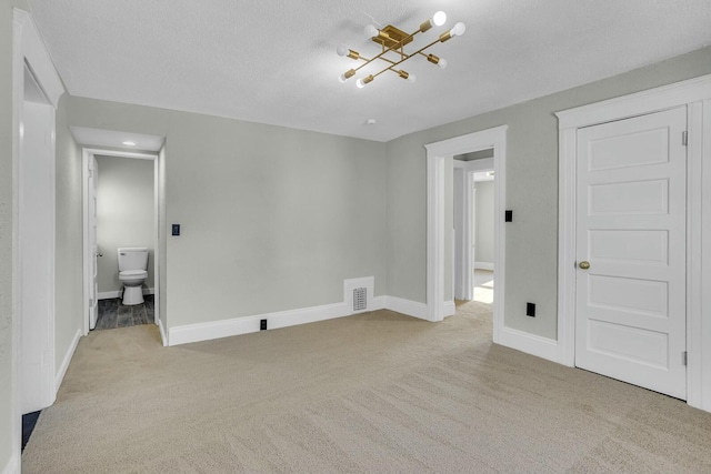 unfurnished bedroom featuring light carpet, a chandelier, a textured ceiling, and ensuite bath