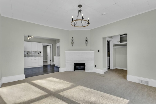 unfurnished living room featuring a brick fireplace, crown molding, a chandelier, and dark colored carpet