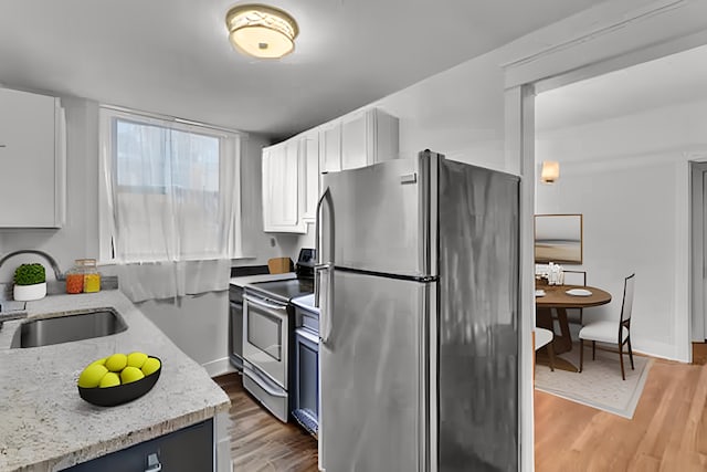 kitchen featuring white cabinets, appliances with stainless steel finishes, light hardwood / wood-style floors, sink, and light stone counters