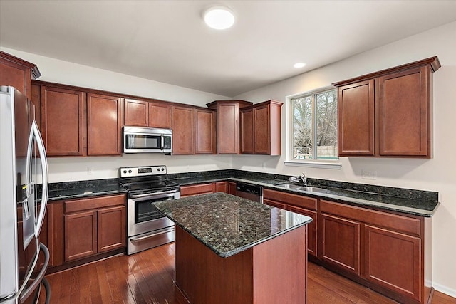 kitchen featuring appliances with stainless steel finishes, dark wood-type flooring, dark stone countertops, a kitchen island, and sink