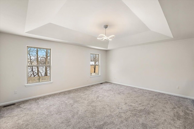 unfurnished room with a wealth of natural light, carpet, a tray ceiling, and a notable chandelier