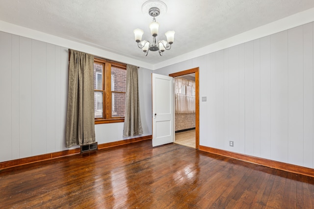 empty room with a chandelier, a textured ceiling, dark wood-style flooring, visible vents, and baseboards