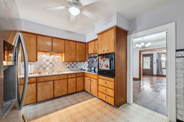 kitchen with decorative light fixtures, tasteful backsplash, a sink, black oven, and stainless steel fridge