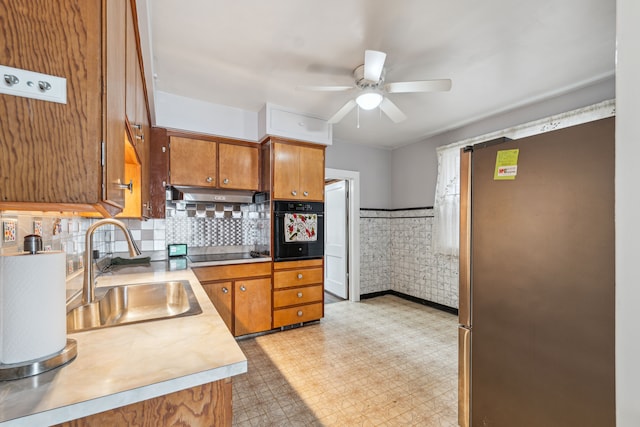 kitchen featuring ceiling fan, under cabinet range hood, a sink, black appliances, and brown cabinetry