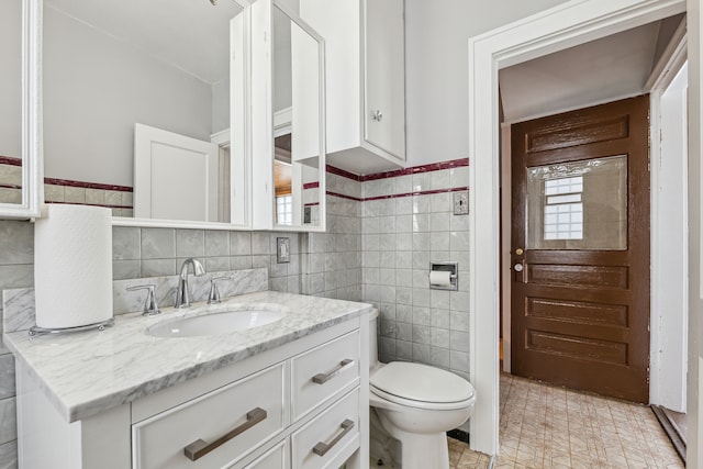 half bathroom with tile walls, wainscoting, vanity, and toilet