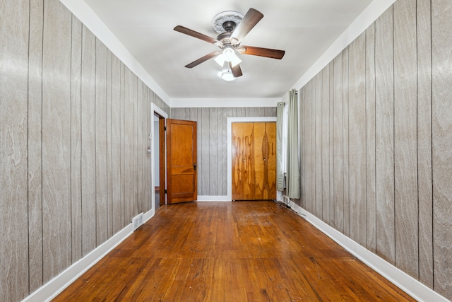 spare room with ceiling fan, wood walls, baseboards, and wood finished floors