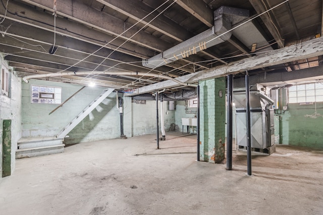 basement with a healthy amount of sunlight, heating unit, stairs, and a sink