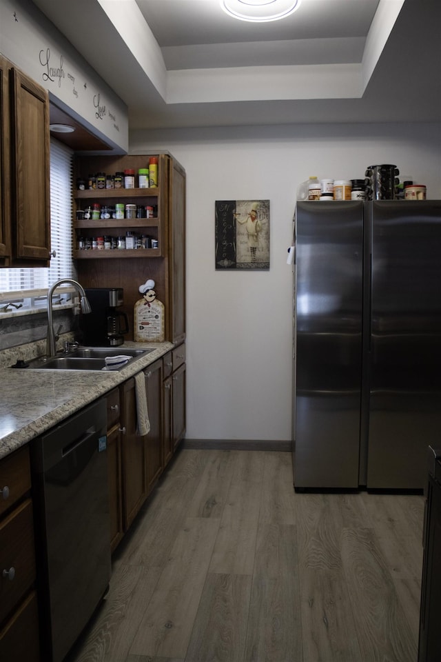 kitchen featuring sink, refrigerator, light wood-type flooring, black dishwasher, and a raised ceiling