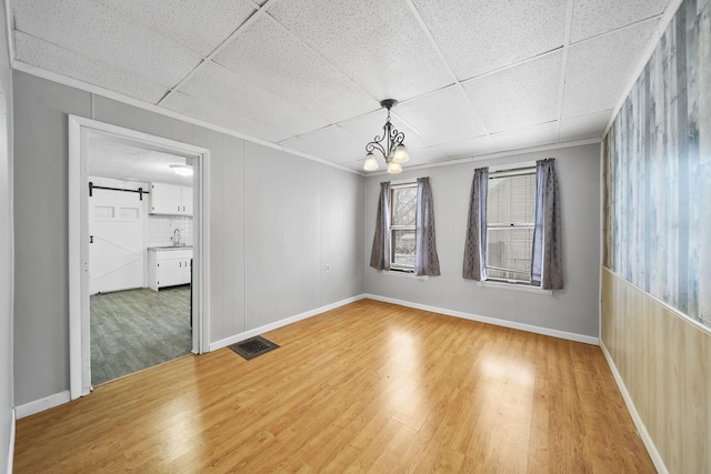 spare room featuring hardwood / wood-style floors, a paneled ceiling, a barn door, and an inviting chandelier