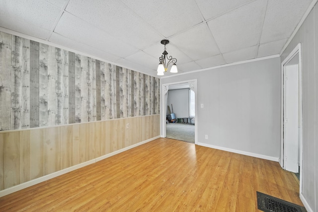 spare room featuring a drop ceiling, wooden walls, a chandelier, and hardwood / wood-style flooring