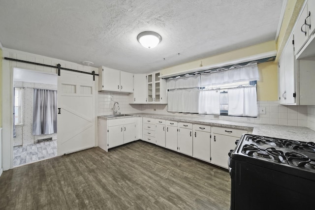 kitchen featuring a barn door, sink, black gas stove, white cabinetry, and dark wood-type flooring