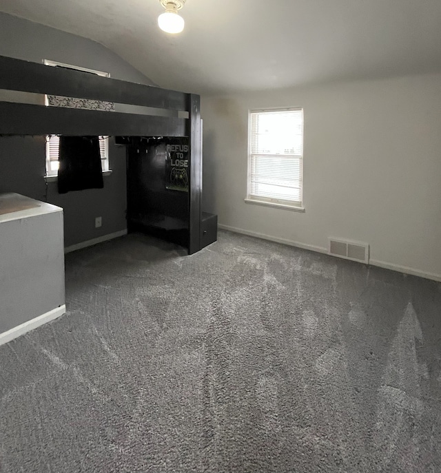 unfurnished bedroom featuring lofted ceiling, multiple windows, and dark colored carpet