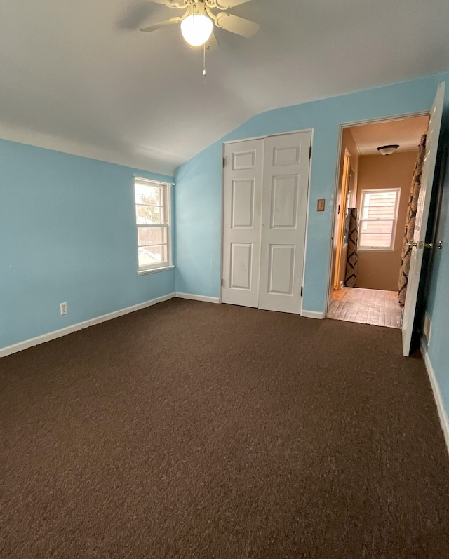 unfurnished bedroom featuring ceiling fan, a closet, dark carpet, and lofted ceiling