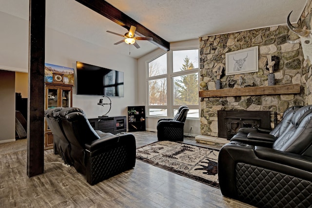 living room with a textured ceiling, hardwood / wood-style floors, a stone fireplace, lofted ceiling with beams, and ceiling fan