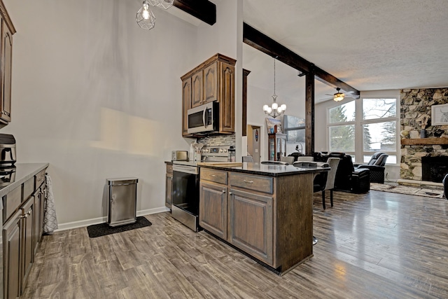 kitchen with a stone fireplace, appliances with stainless steel finishes, a kitchen breakfast bar, wood-type flooring, and lofted ceiling with beams