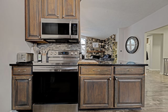 kitchen with appliances with stainless steel finishes, backsplash, lofted ceiling, dark stone counters, and light hardwood / wood-style flooring