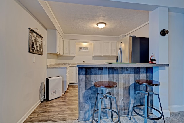 kitchen with a kitchen breakfast bar, white cabinetry, crown molding, and stainless steel refrigerator