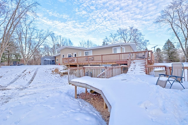 snow covered rear of property featuring a deck and a storage unit