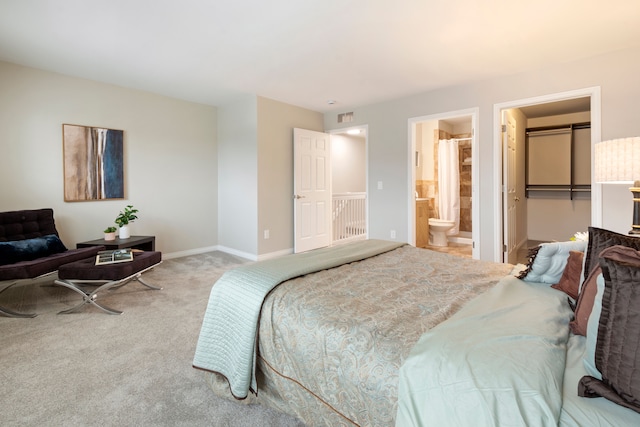 bedroom featuring a spacious closet, light colored carpet, a closet, and ensuite bath