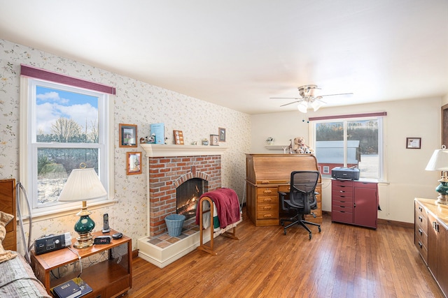 office area with ceiling fan, a brick fireplace, dark hardwood / wood-style floors, and a wealth of natural light