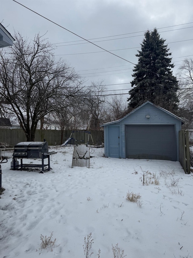 yard layered in snow with a playground, a garage, and an outbuilding