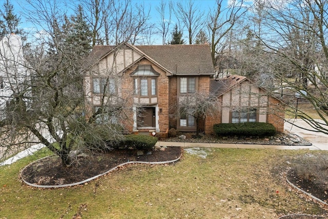 english style home featuring brick siding, a front yard, and a shingled roof