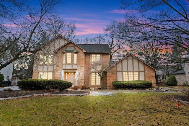 english style home featuring a front lawn, brick siding, roof with shingles, and stucco siding