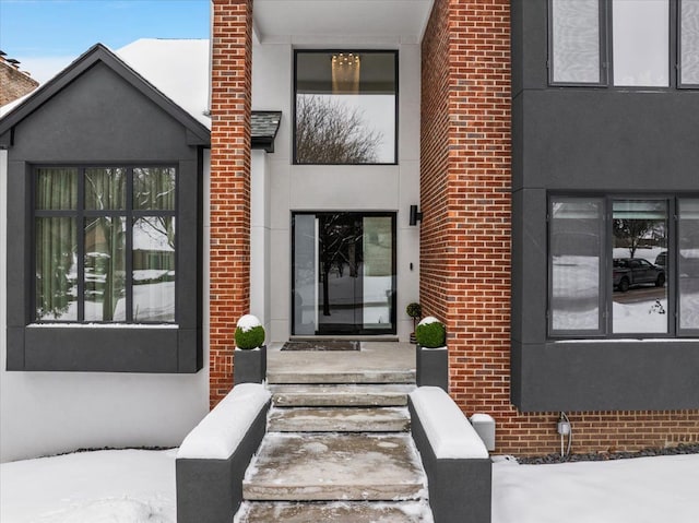 snow covered property entrance with brick siding and stucco siding