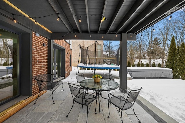 snow covered patio featuring outdoor dining space, a trampoline, and a covered hot tub