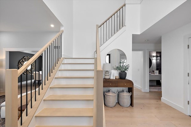 staircase featuring a high ceiling, baseboards, and wood finished floors