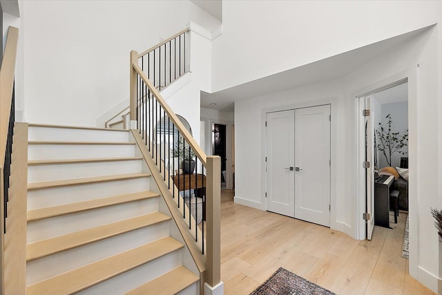 stairs featuring wood finished floors, a towering ceiling, and baseboards