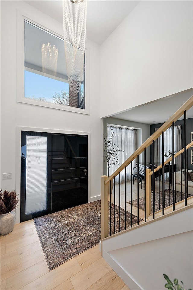 foyer with stairs, a high ceiling, wood finished floors, and a notable chandelier