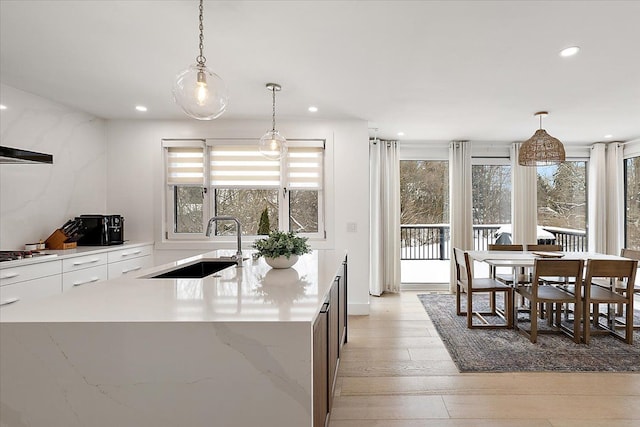 kitchen featuring a kitchen island with sink, hanging light fixtures, a sink, and white cabinetry