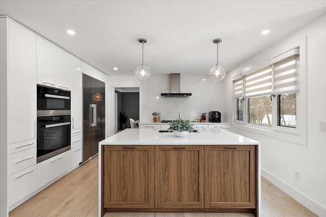 kitchen featuring hanging light fixtures, wall chimney range hood, light countertops, and white cabinets