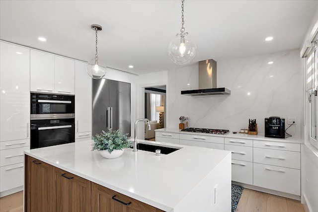 kitchen featuring light countertops, wall chimney range hood, appliances with stainless steel finishes, and a center island with sink