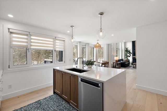 kitchen with dishwasher, an island with sink, open floor plan, light countertops, and a sink