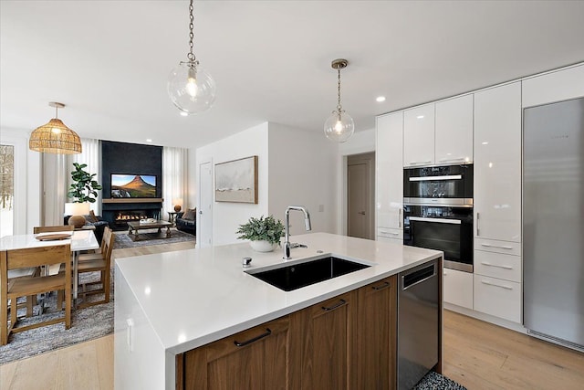 kitchen with a center island with sink, open floor plan, white cabinetry, a sink, and dishwashing machine