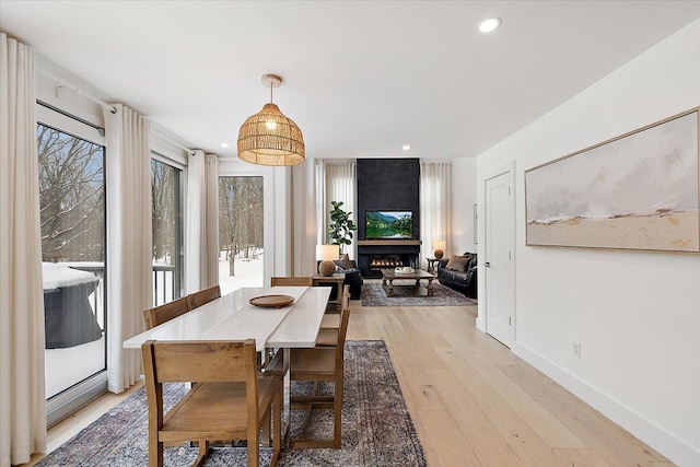 dining space featuring a large fireplace, light wood finished floors, baseboards, and recessed lighting