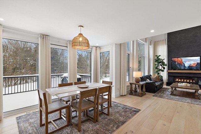 dining room featuring visible vents, a glass covered fireplace, a wealth of natural light, and light wood-style floors