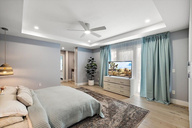 bedroom featuring light wood-style floors, baseboards, visible vents, and a raised ceiling