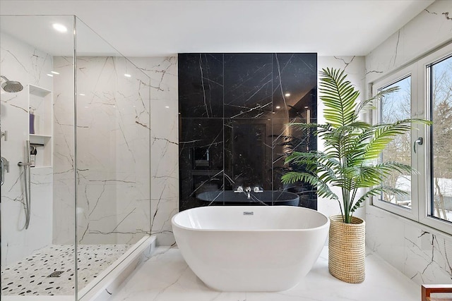 bathroom with marble finish floor, tile walls, a marble finish shower, a soaking tub, and stone wall