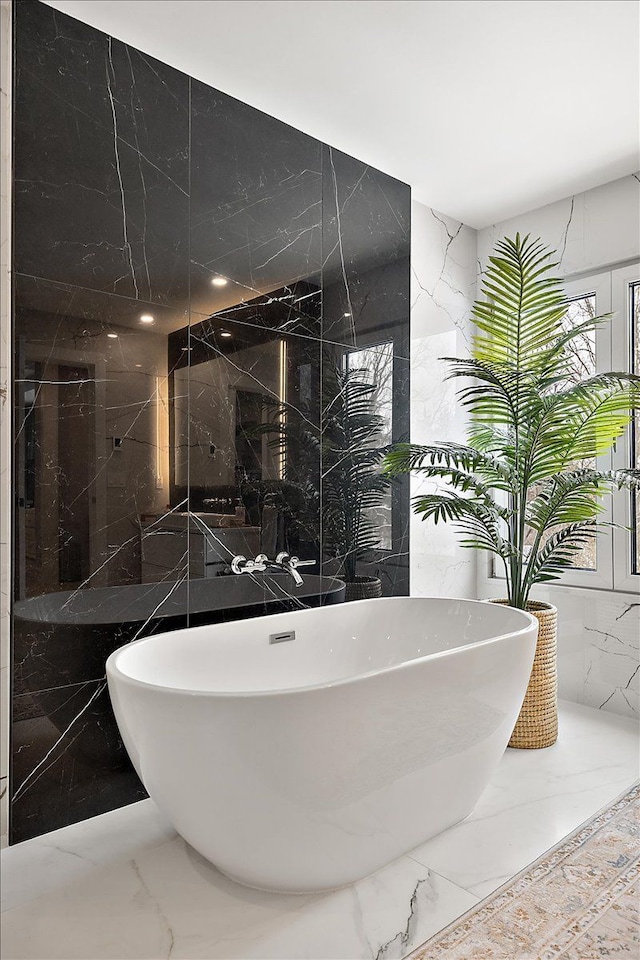 bathroom with marble finish floor, stone wall, a freestanding bath, and tile walls