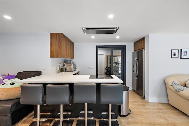 kitchen featuring brown cabinetry, stainless steel fridge with ice dispenser, open floor plan, a peninsula, and light countertops