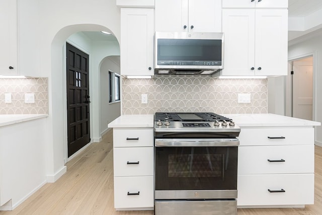 kitchen featuring light hardwood / wood-style flooring, appliances with stainless steel finishes, white cabinetry, light stone counters, and decorative backsplash