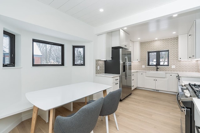 kitchen with appliances with stainless steel finishes, white cabinetry, decorative backsplash, sink, and light hardwood / wood-style flooring