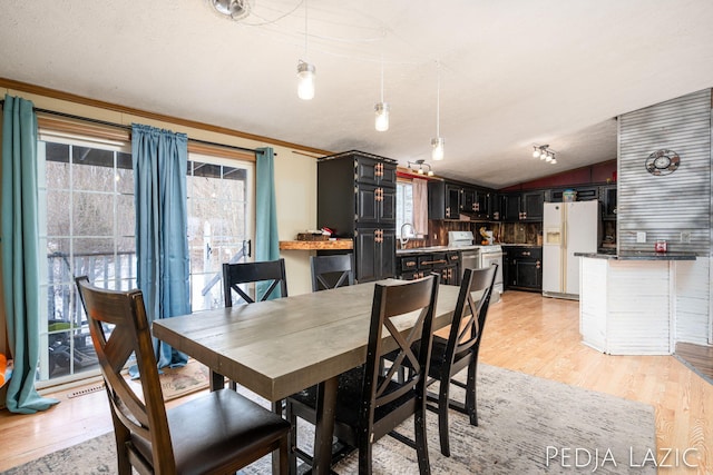 dining space featuring vaulted ceiling, a textured ceiling, light hardwood / wood-style floors, and plenty of natural light