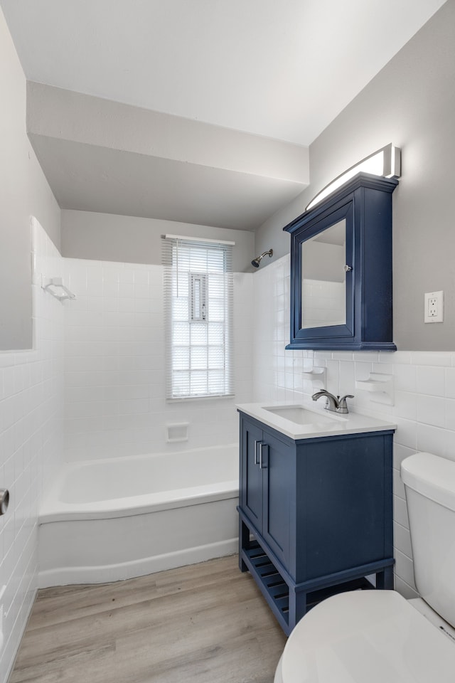 full bathroom with toilet, tiled shower / bath, tile walls, vanity, and hardwood / wood-style flooring