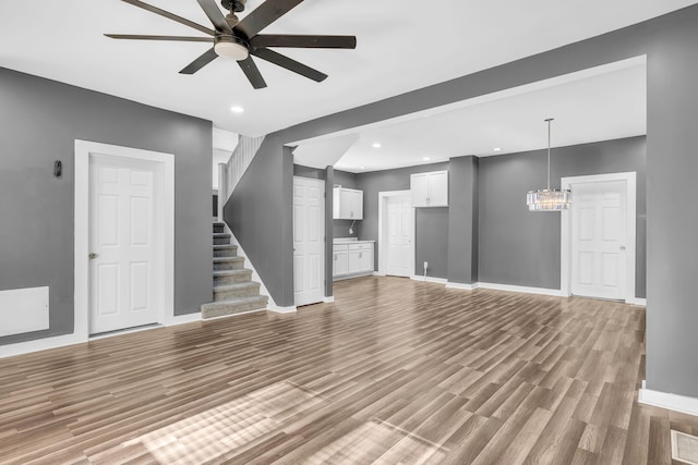 unfurnished living room with ceiling fan with notable chandelier and light hardwood / wood-style flooring