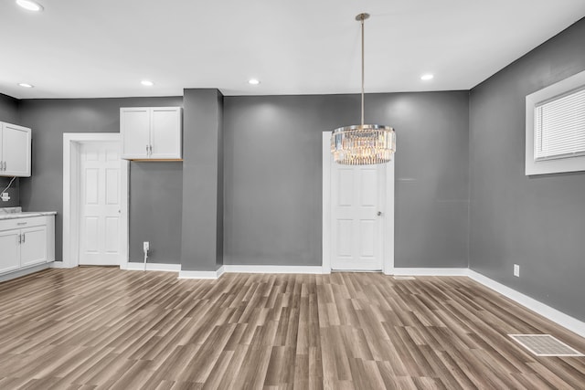 unfurnished dining area featuring light wood-type flooring and an inviting chandelier